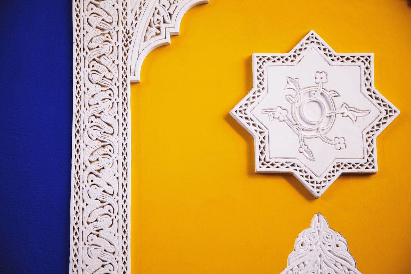 Intricate carvings in white plaster on a blue and yellow wall.